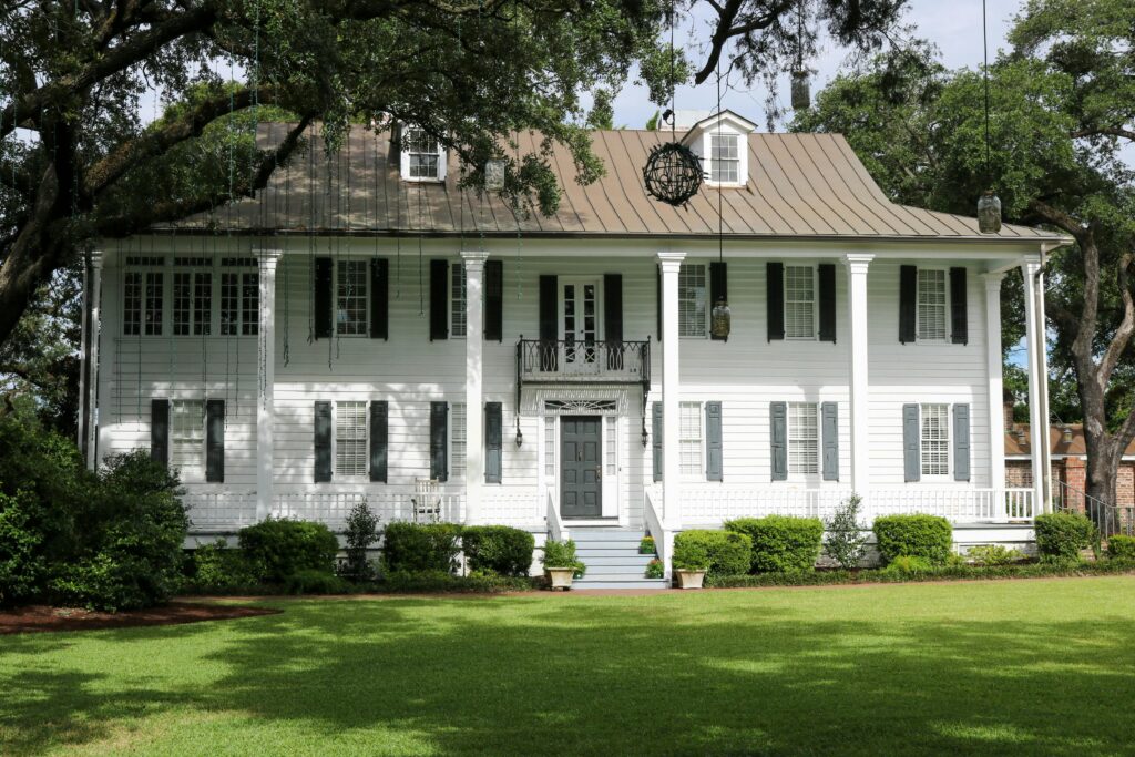 Elegant colonial house with lush lawn and classic facade surrounded by trees.